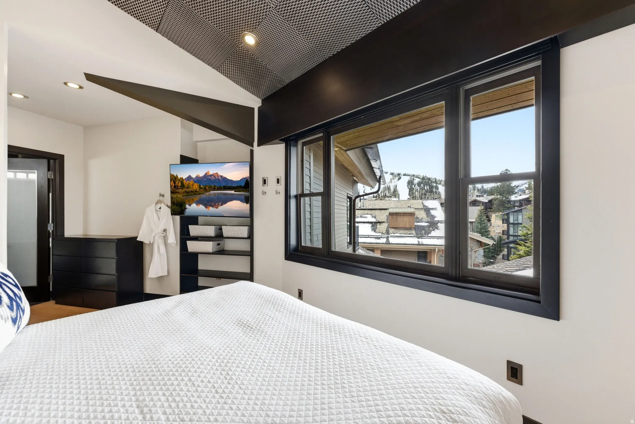 Modern bedroom featuring large dark-framed windows, a built-in entertainment center, recessed lighting, and a textured ceiling