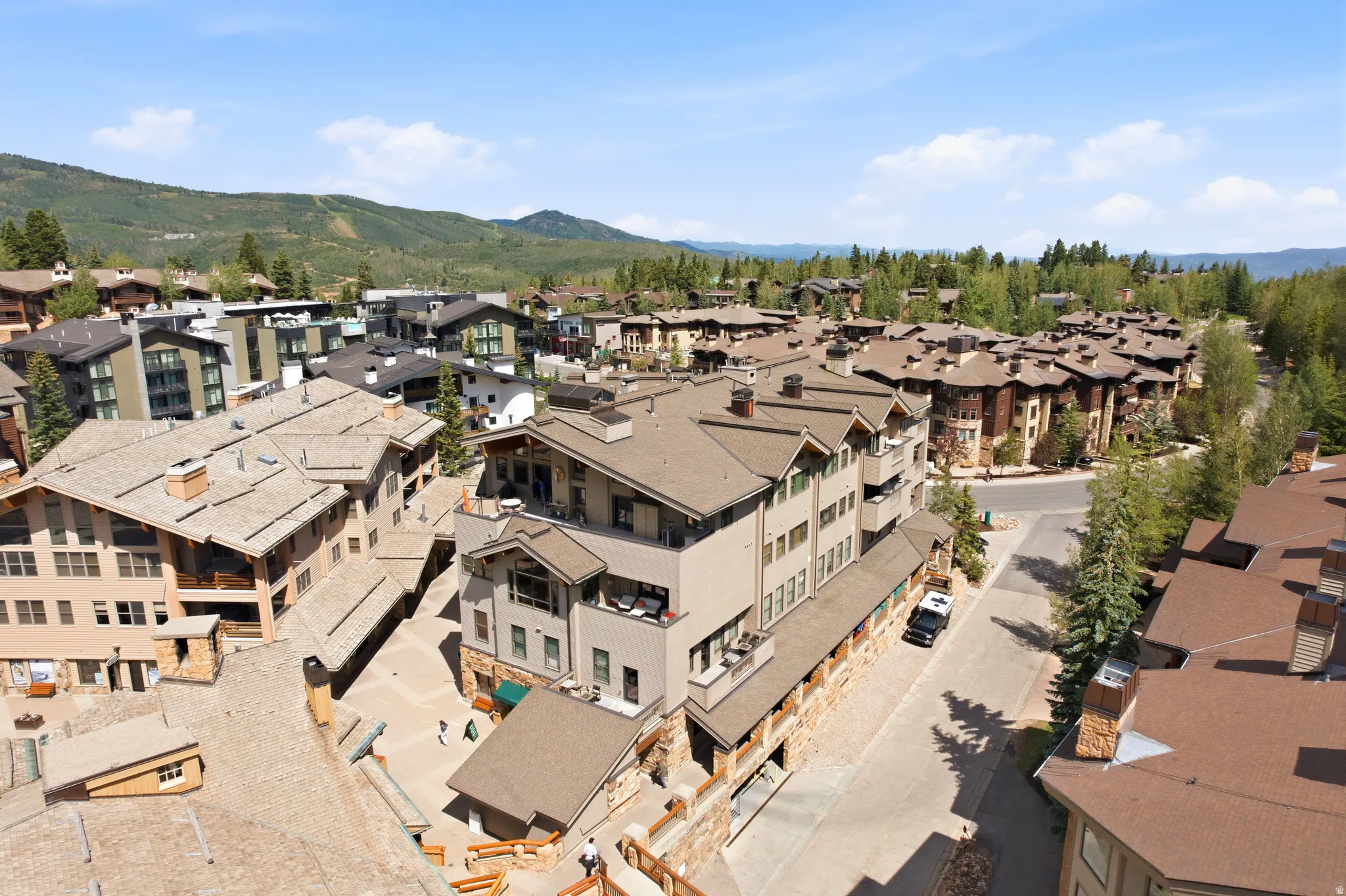 Aerial perspective showcasing a community of multi-story buildings with varied architectural styles, nestled in a mountainous landscape
