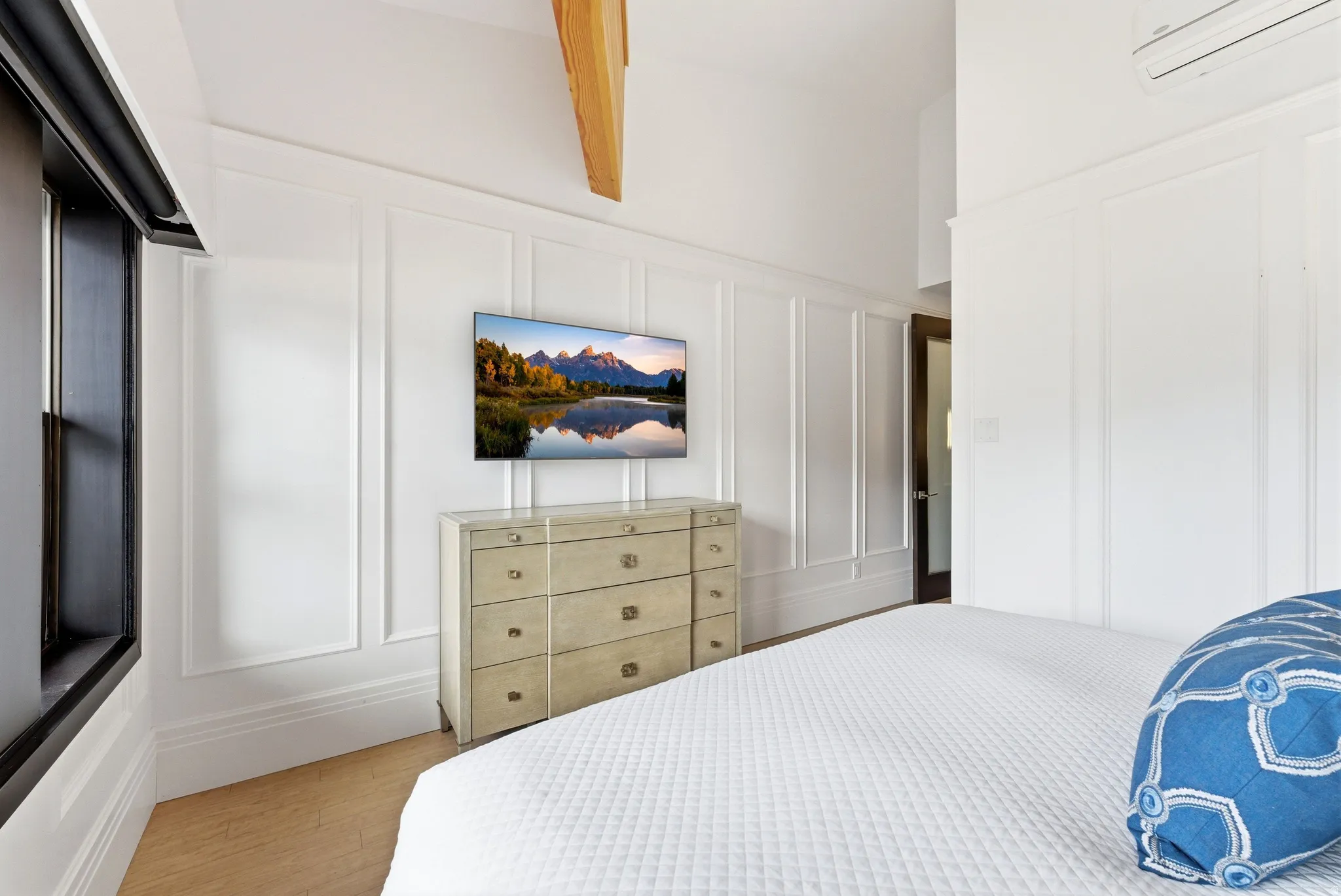 White paneled walls featuring tall baseboards, wood-finish flooring, and a dark-framed window