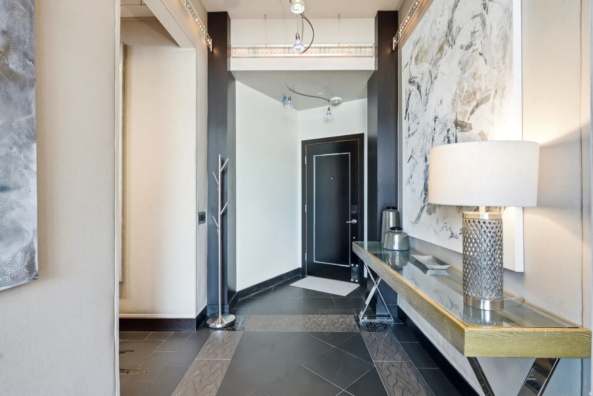 Entryway featuring dark tile flooring with patterned accents, contrasting white and dark accent walls, and a recessed ceiling with track lighting