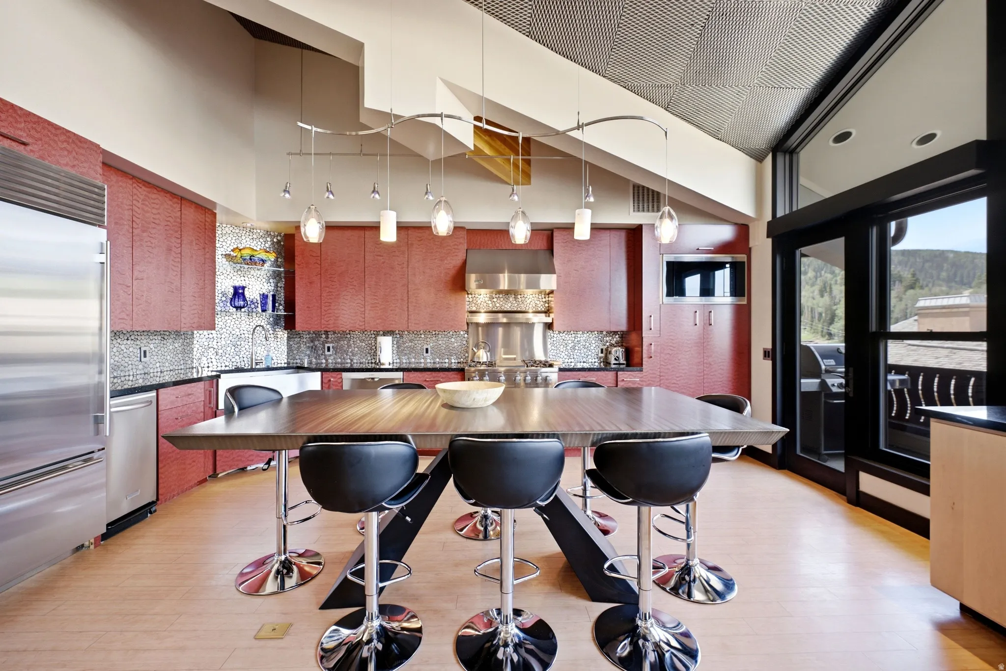 Open-concept kitchen featuring red textured cabinetry, stainless steel appliances, and a mosaic tile backsplash