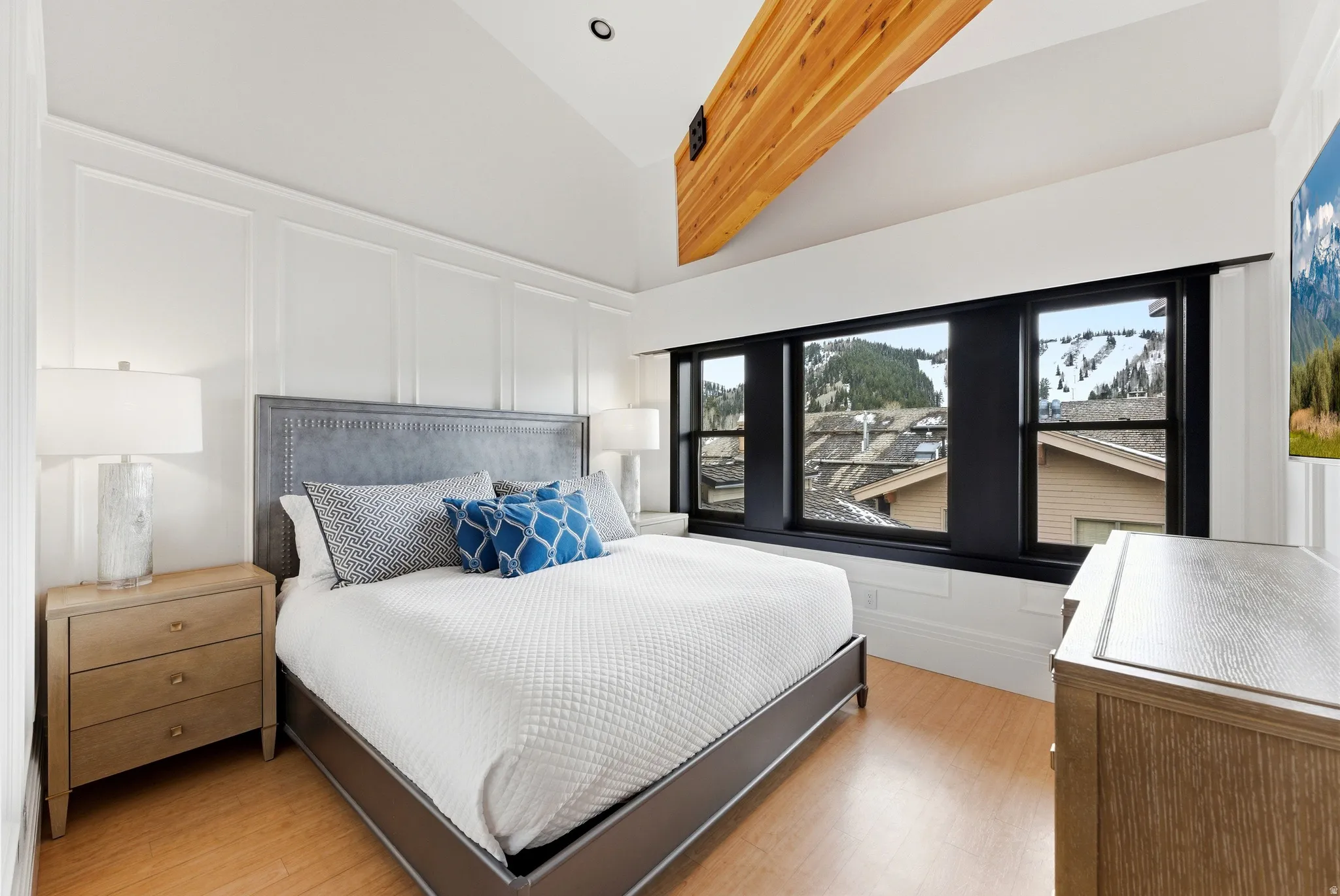 Bedroom featuring a vaulted ceiling with exposed wood beam, wainscoting, and wood-finish flooring