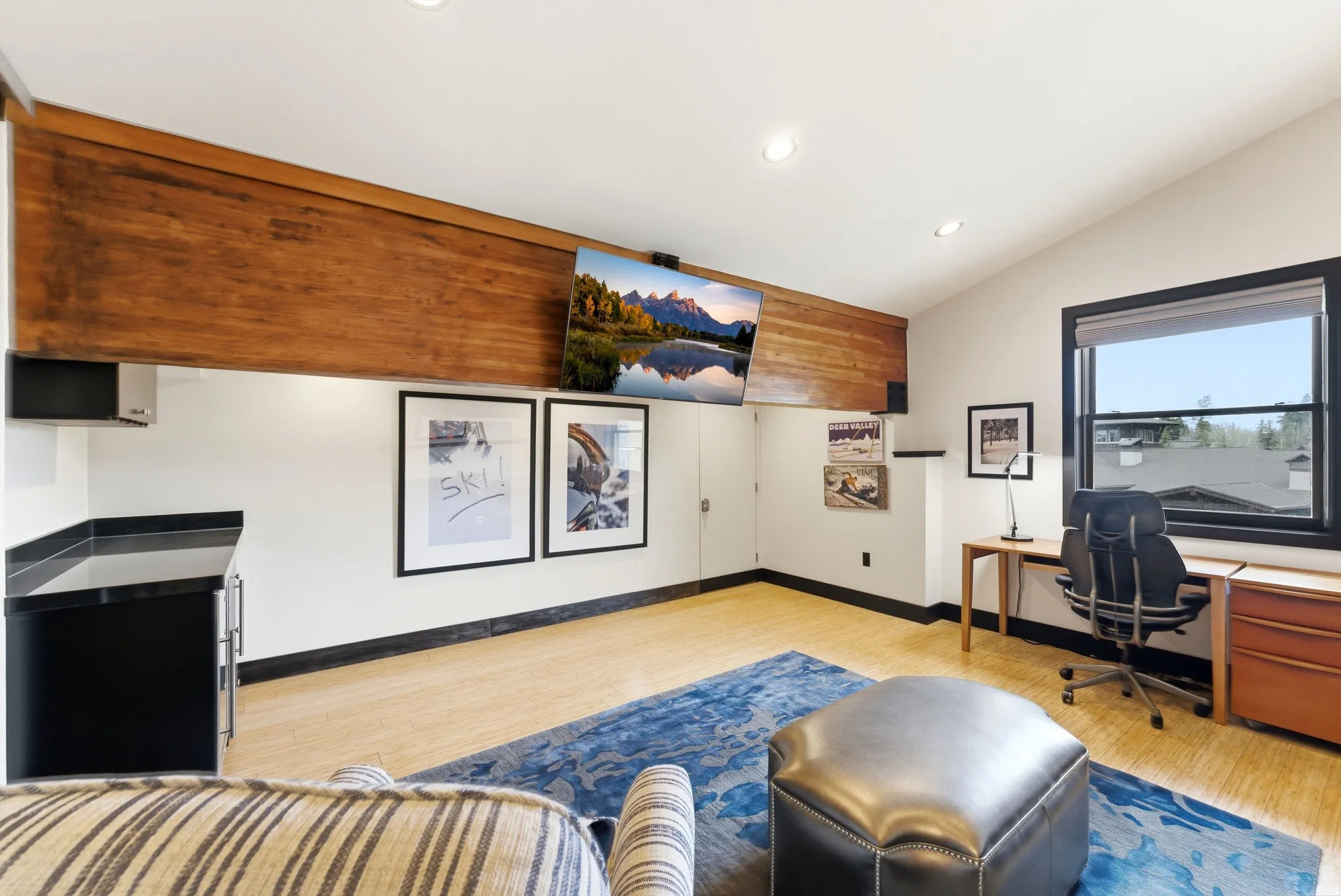 Vaulted ceiling room featuring light-toned flooring, a built-in wet bar with a dark countertop and under-counter refrigeration, and a prominent wood-paneled beam
