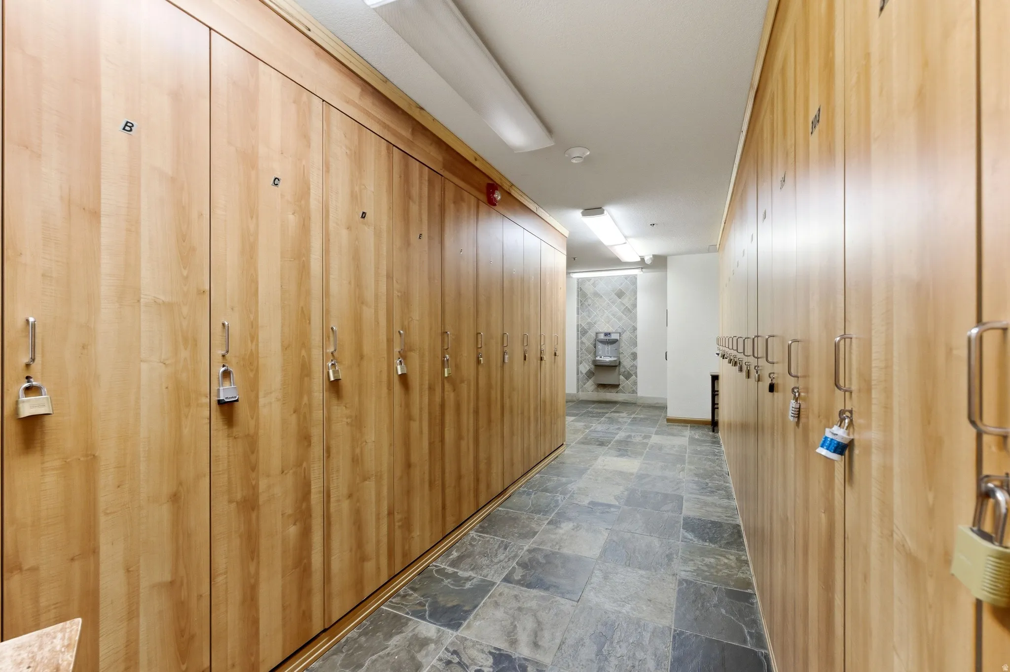 Corridor featuring extensive wood-finish locker storage, slate-style floor tiling, recessed lighting, and a built-in water fountain