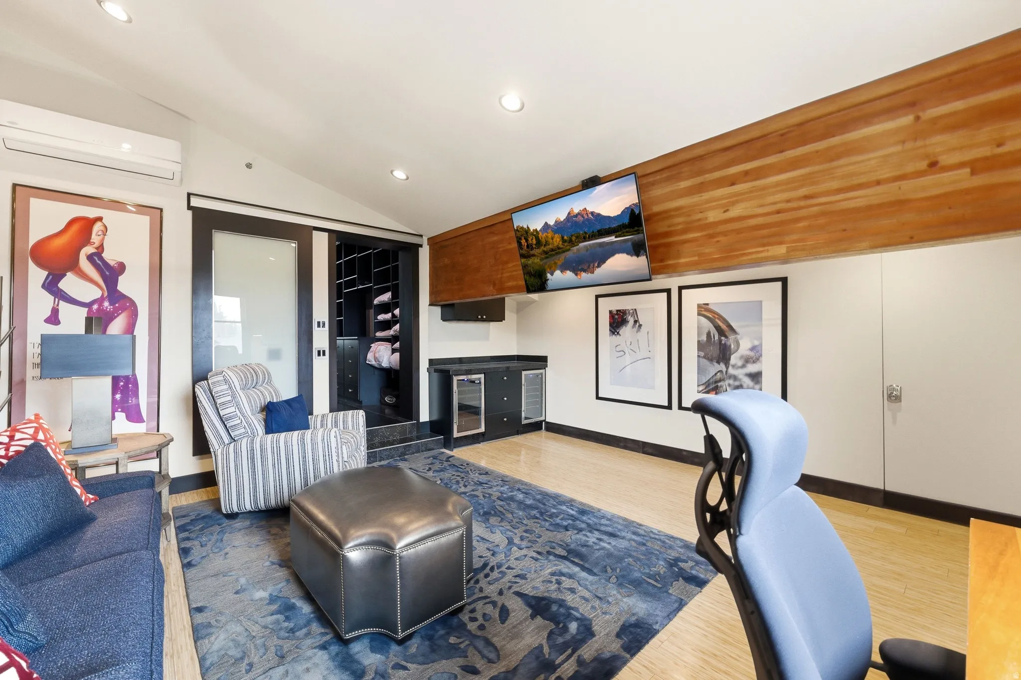 Vaulted ceiling room featuring light wood-finish flooring, a built-in wet bar with integrated refrigeration, and a custom built-in closet with sliding glass panel doors