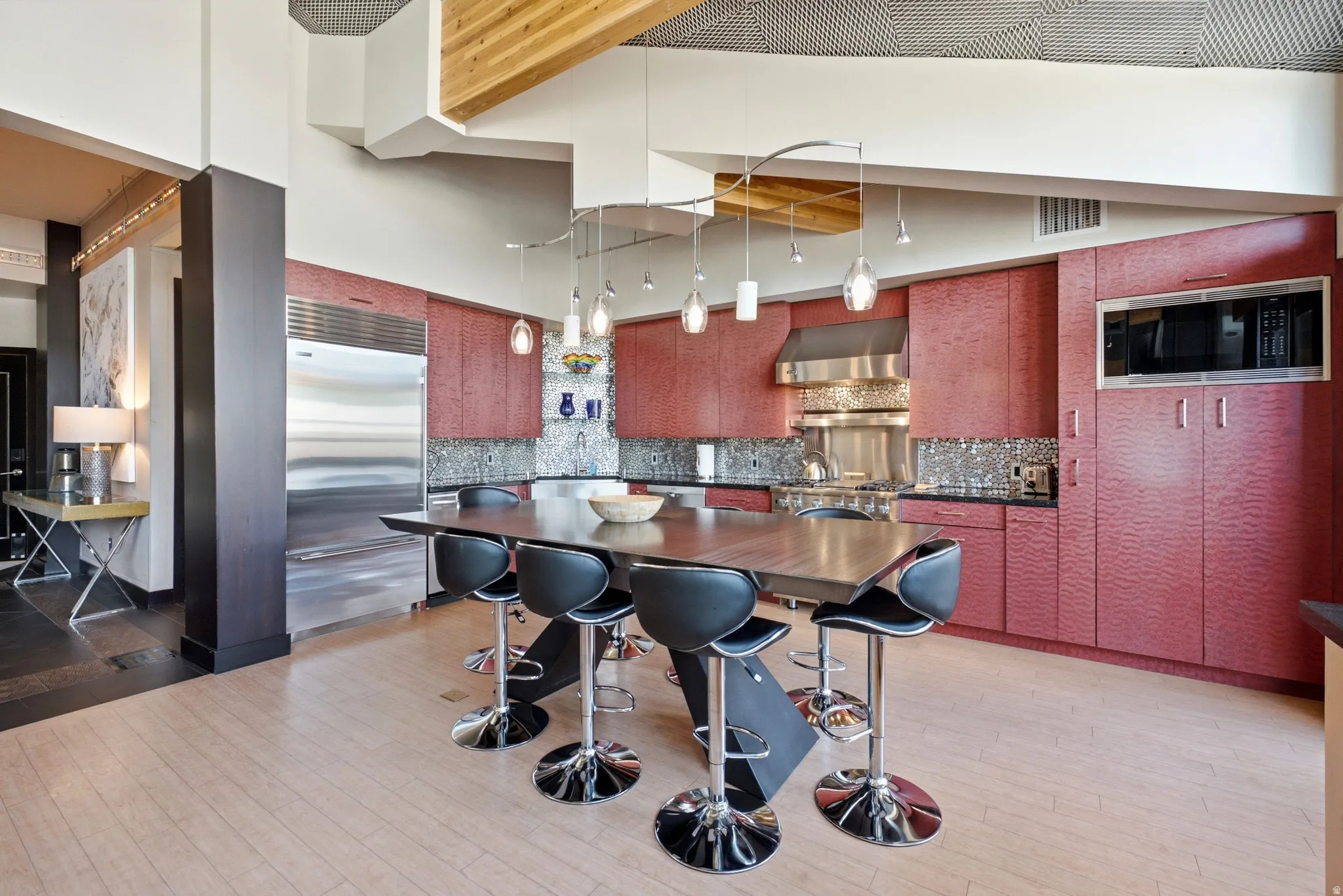 Contemporary kitchen featuring a large central island with seating, a stainless steel built-in refrigerator, integrated double ovens, and a matching range hood
