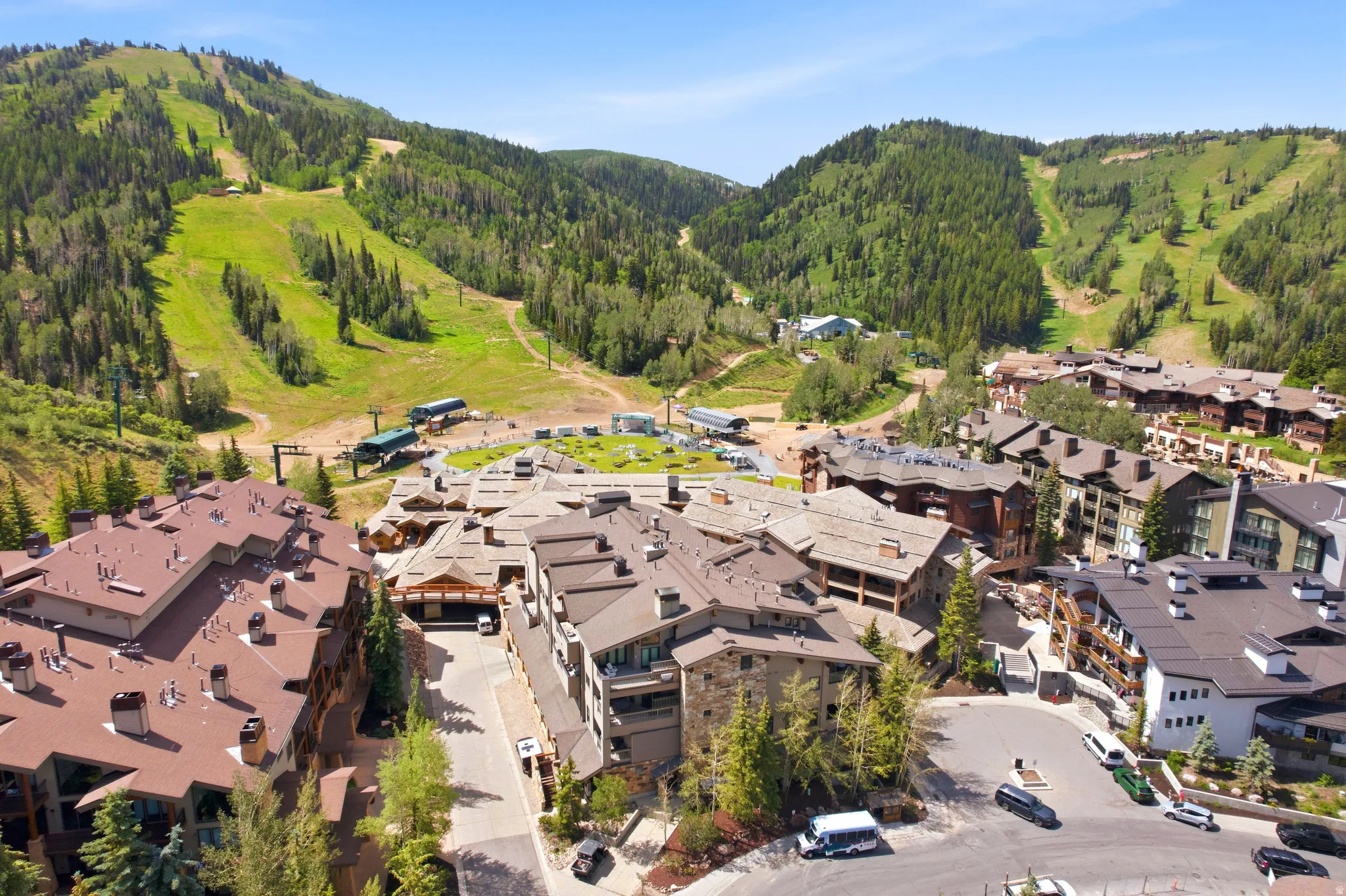 Mountain resort property featuring multiple buildings with varied architectural styles, nestled against a backdrop of lush green slopes and dense forest
