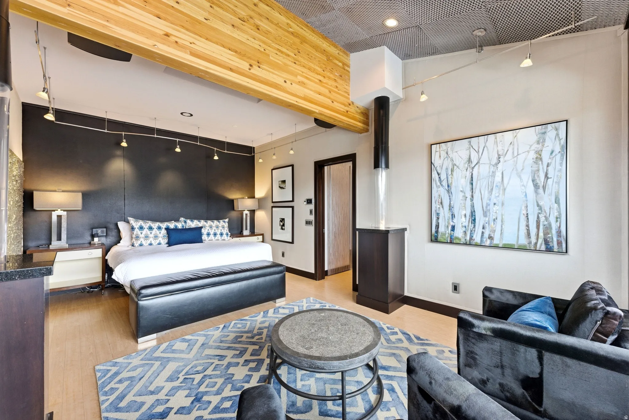 Bedroom featuring wood-finish flooring, exposed wood beam ceiling, track lighting, a dark accent wall, and a built-in vertical water feature