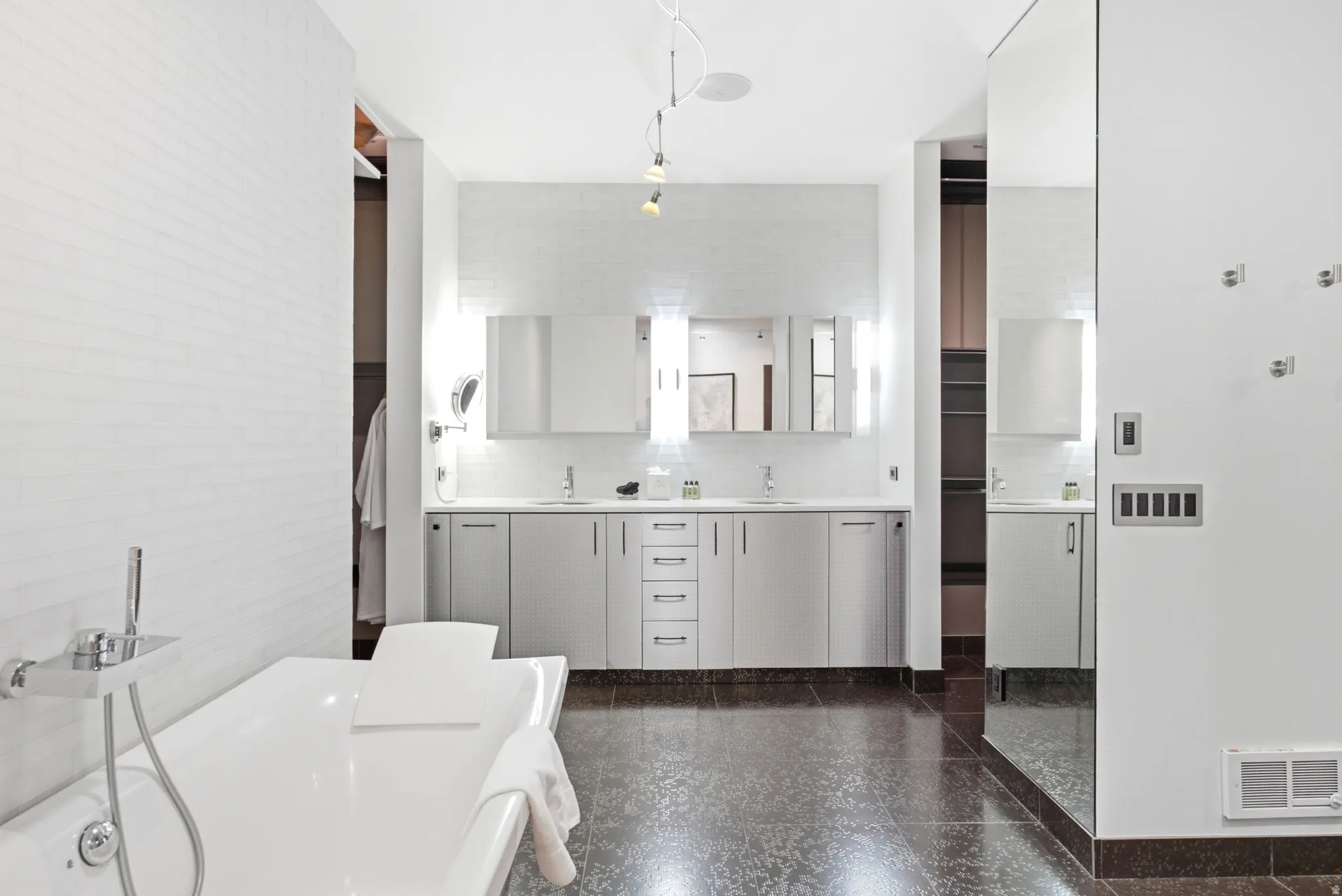 Contemporary bathroom featuring a freestanding tub with chrome fixtures, dual vanities with integrated sinks, modern cabinetry, and dark-toned flooring