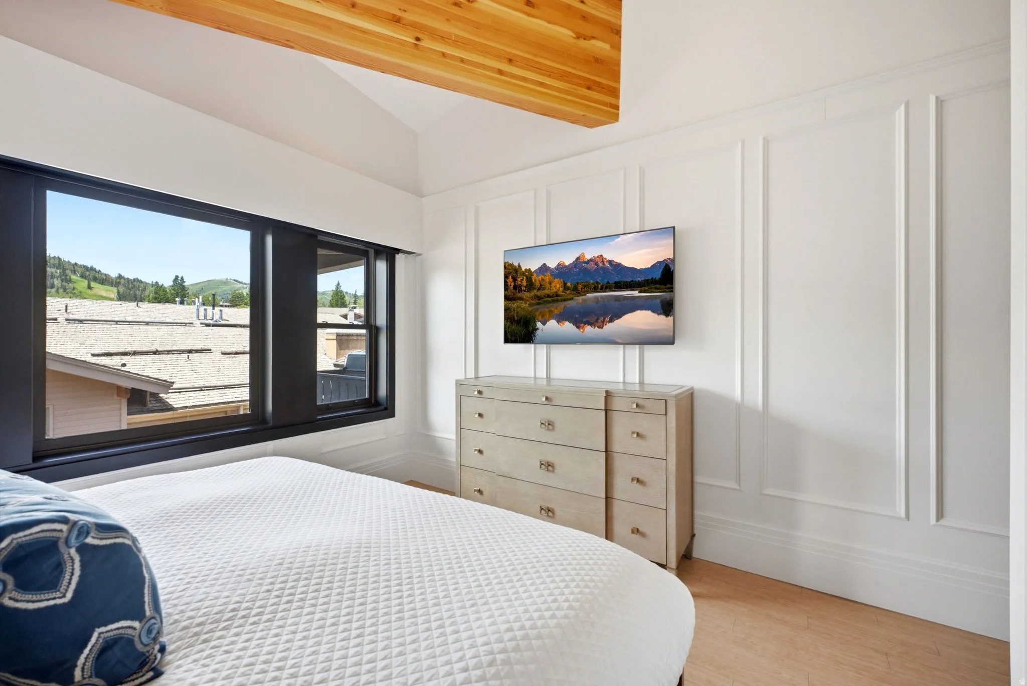 Room with wood-finish flooring, a vaulted ceiling with exposed wood beams, and a window with black trim