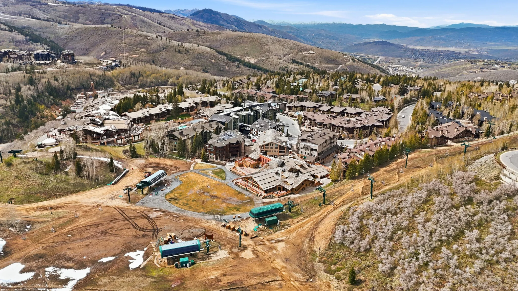 Expansive mountain community showcasing numerous residential structures, substantial natural landscaping, a winding paved road, and ski lift infrastructure