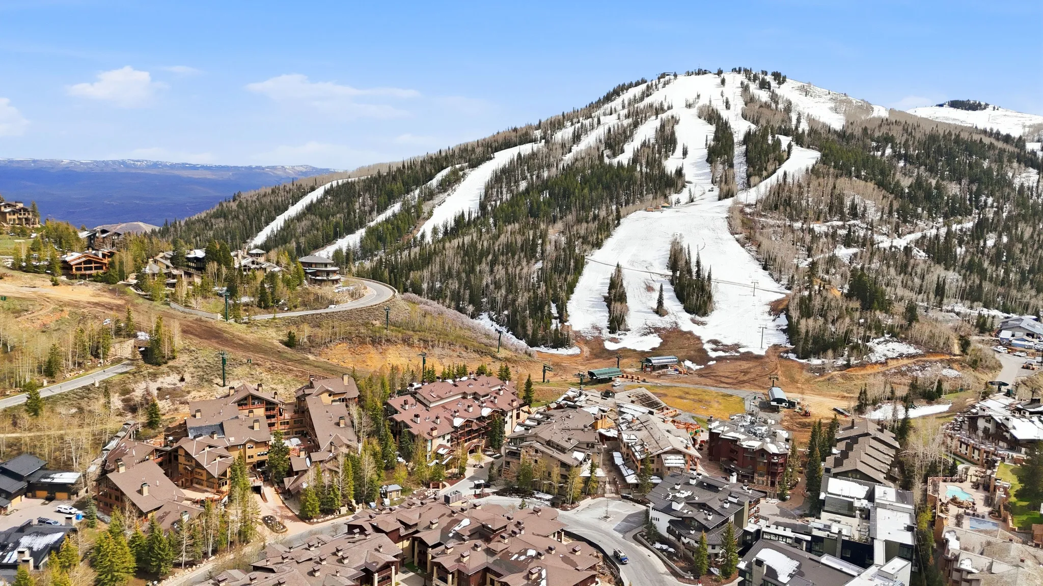 Mountainous terrain featuring ski slopes with remaining snow, surrounded by evergreen and deciduous trees