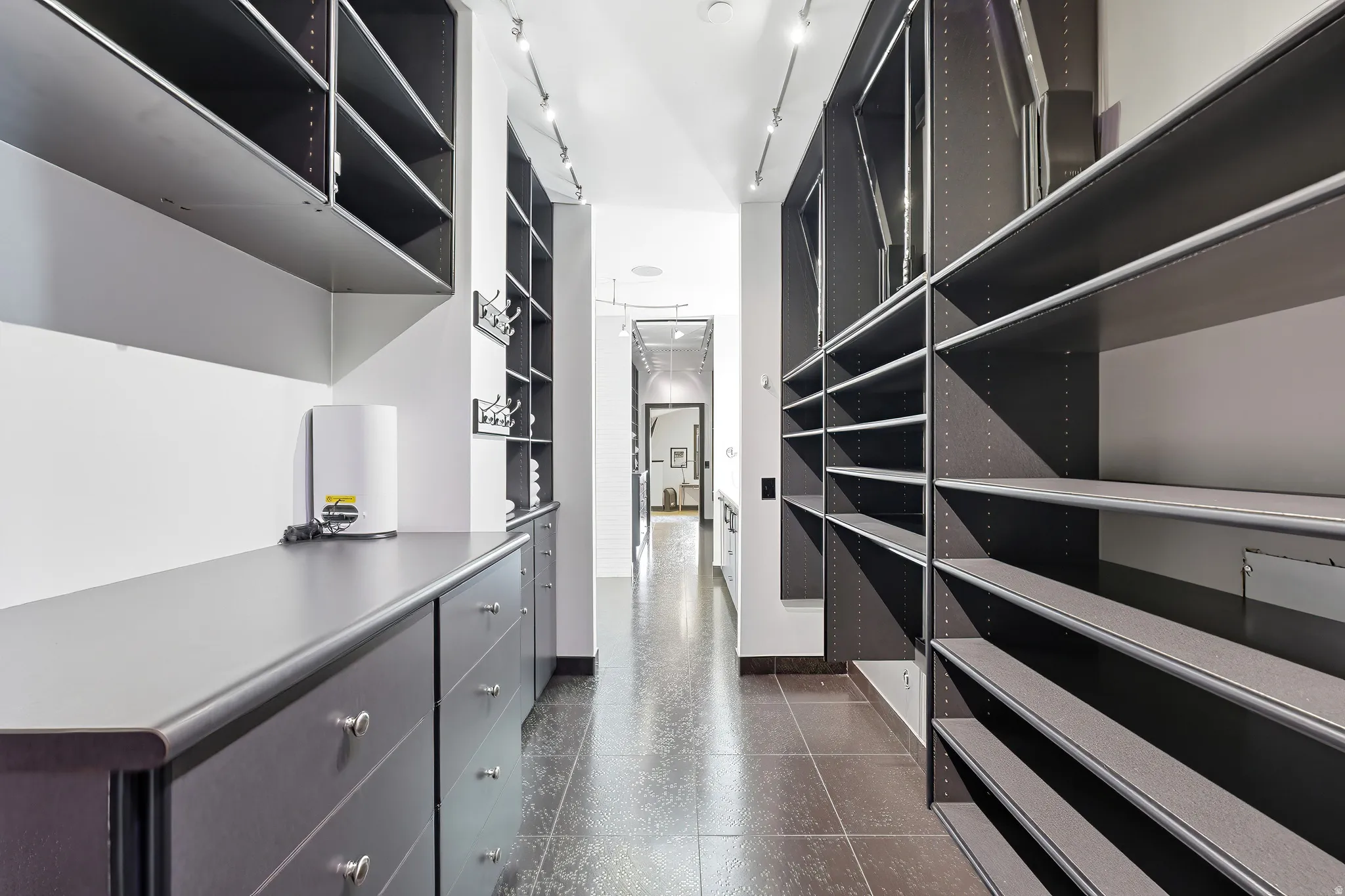 Expansive custom closet system featuring extensive shelving, integrated drawers, track lighting, and durable tile flooring
