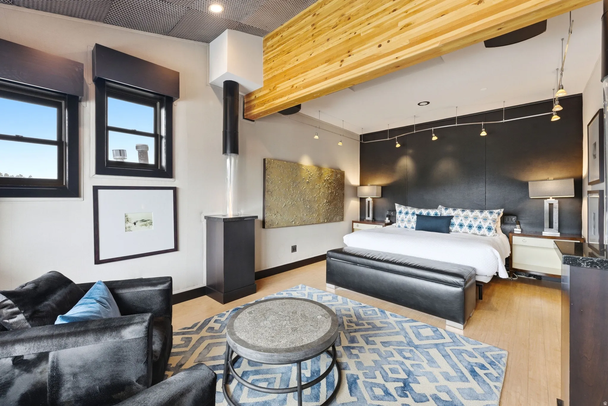 Hardwood-finish flooring featuring a dark accent wall, two windows with dark trim, a built-in ethanol fireplace, and exposed wood beam ceiling details