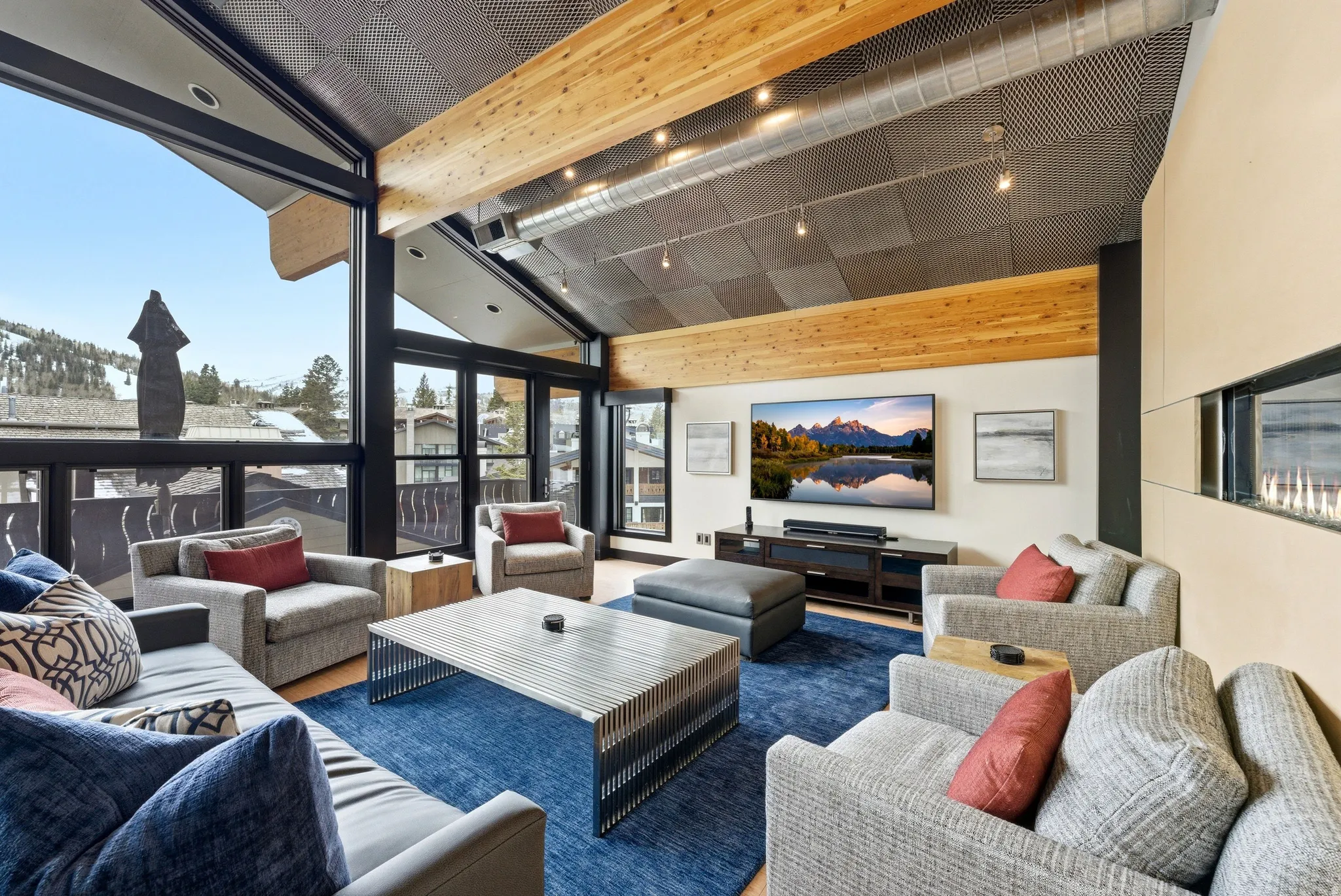 Living area featuring expansive windows, a contemporary linear fireplace, exposed wood beams, and a vaulted ceiling with track lighting
