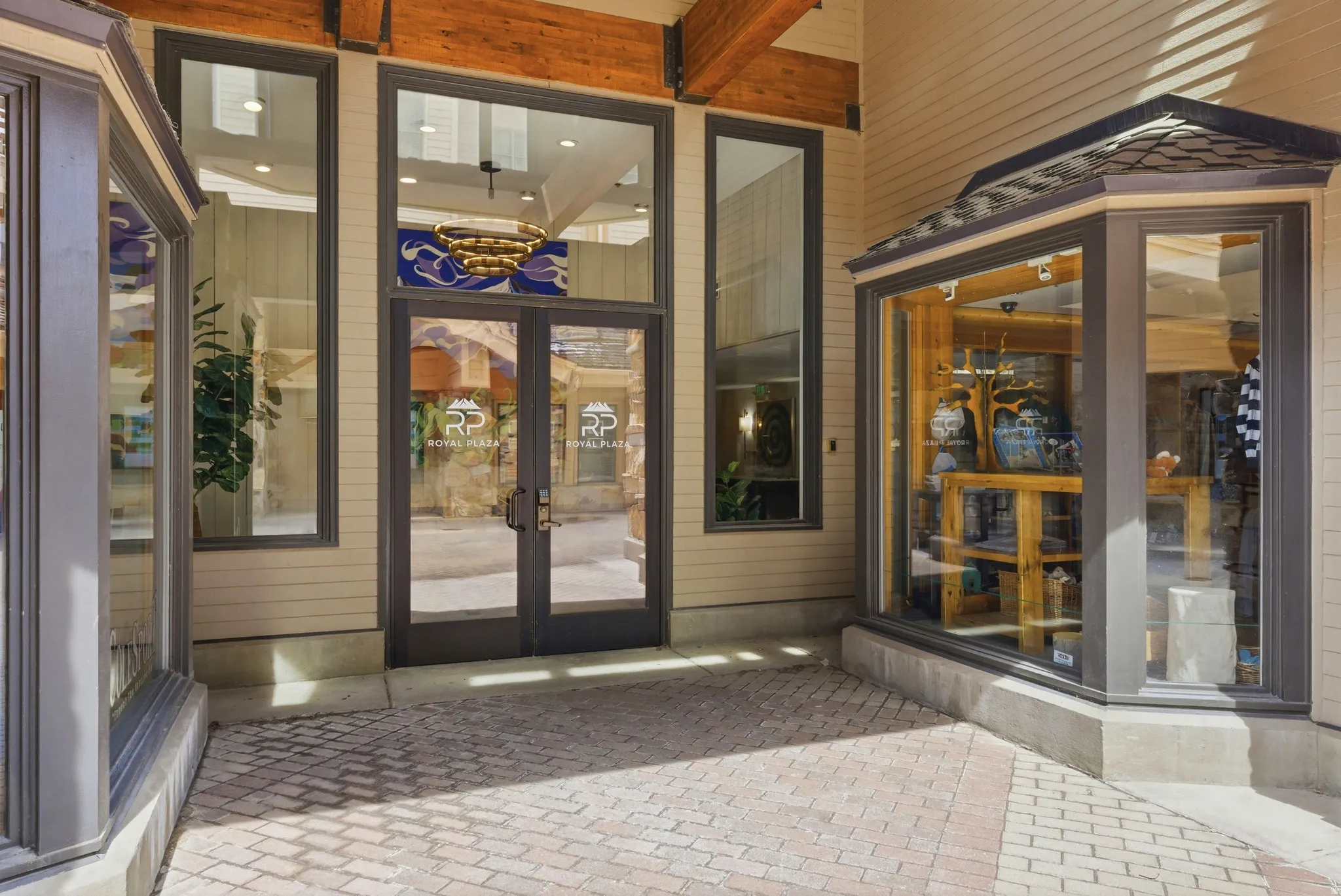Commercial entryway featuring large glass doors, extensive window frontage, exposed timber beams, and a brick paver pathway