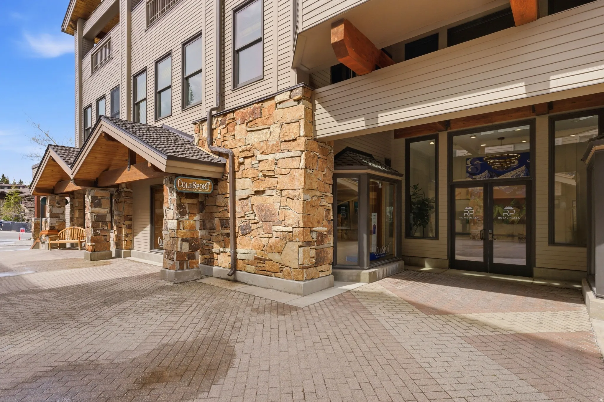 Multi-story building exterior featuring a stone and siding facade, stone column supports, exposed wood beams, and a paved brick entrance