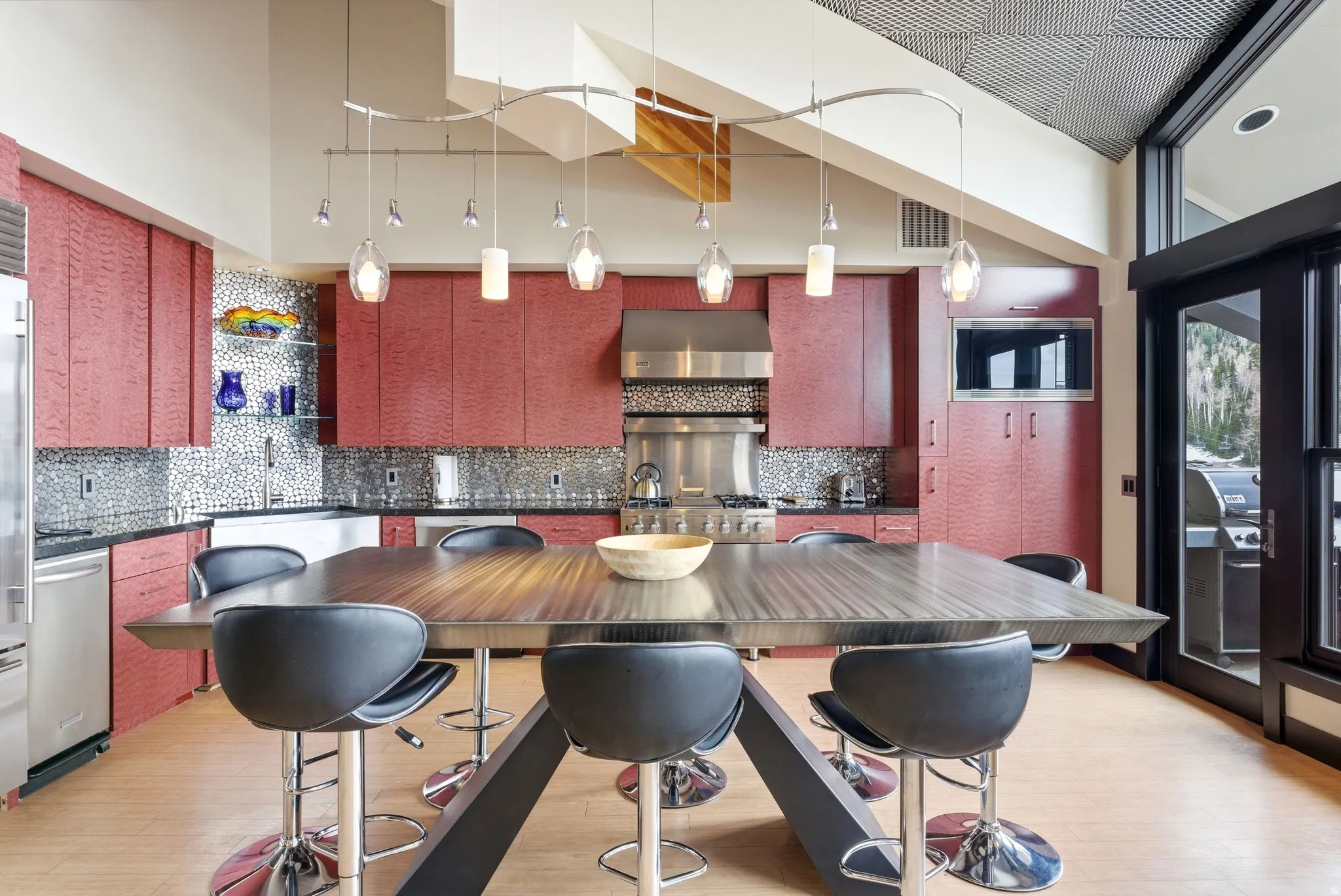 Contemporary kitchen featuring red cabinetry, a mosaic tile backsplash, black countertops, and stainless steel appliances