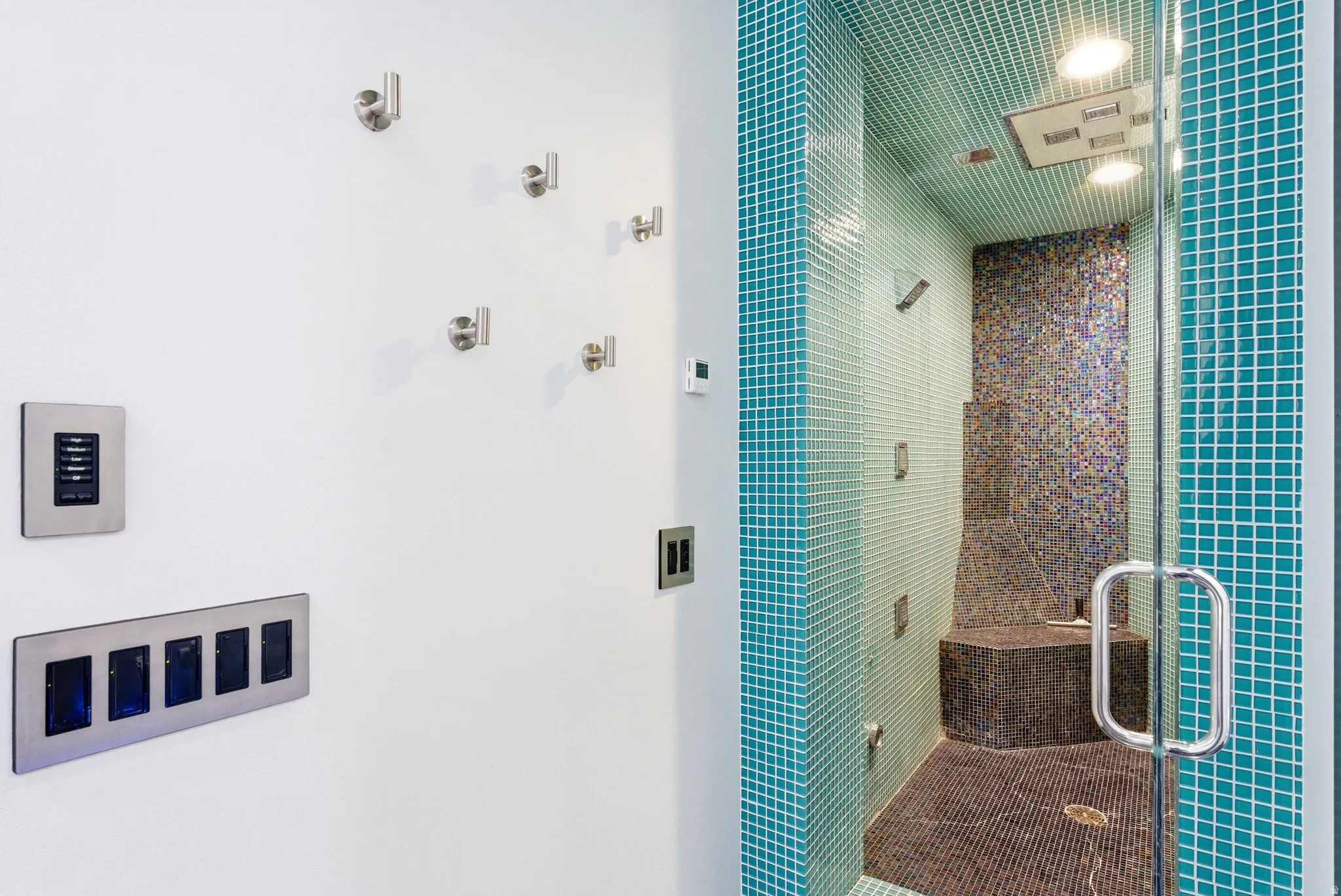 Tiled shower enclosure featuring a glass door and multiple shower heads