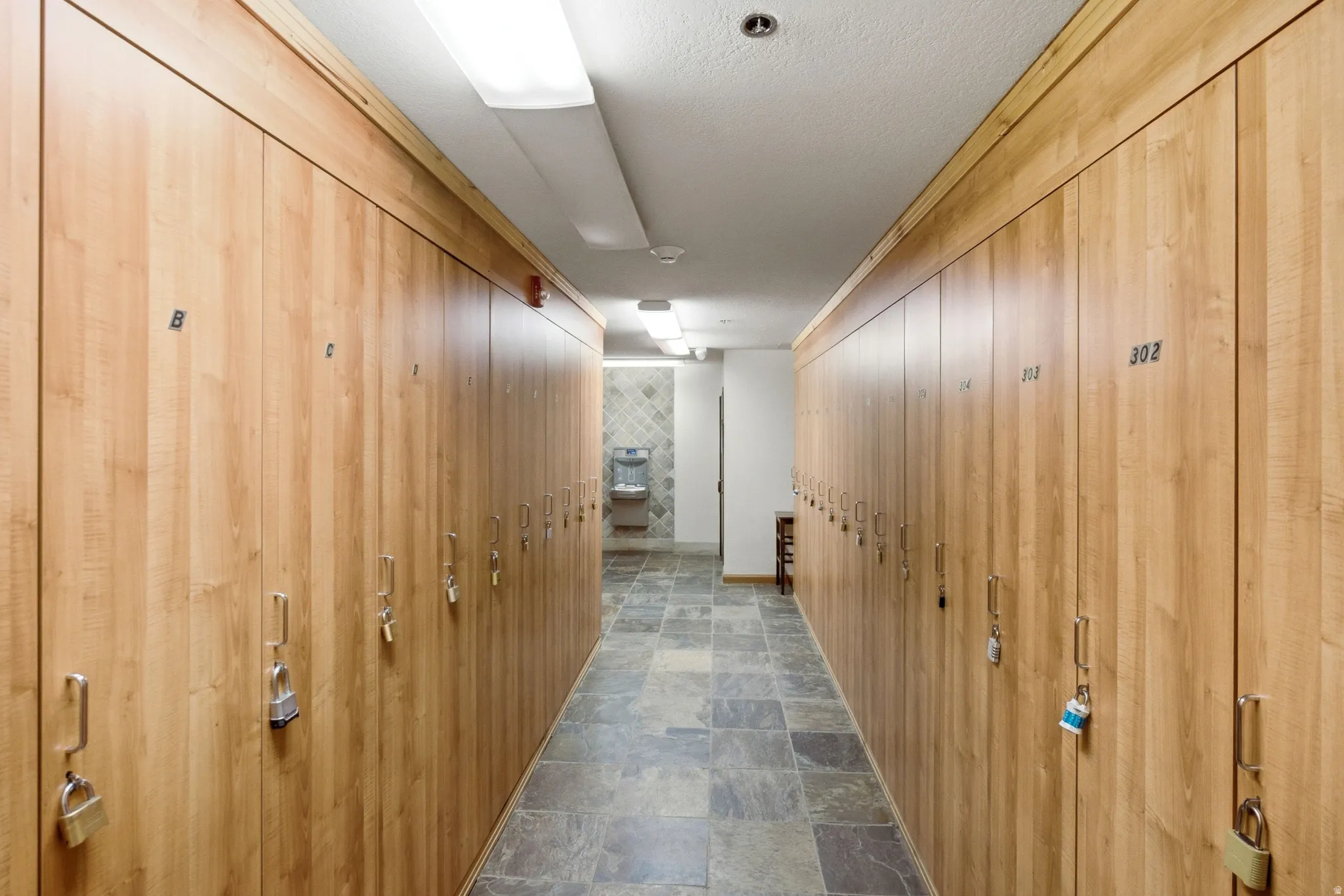 Corridor featuring extensive wood-finish locker storage, square tile flooring, a water fountain, and recessed ceiling lighting