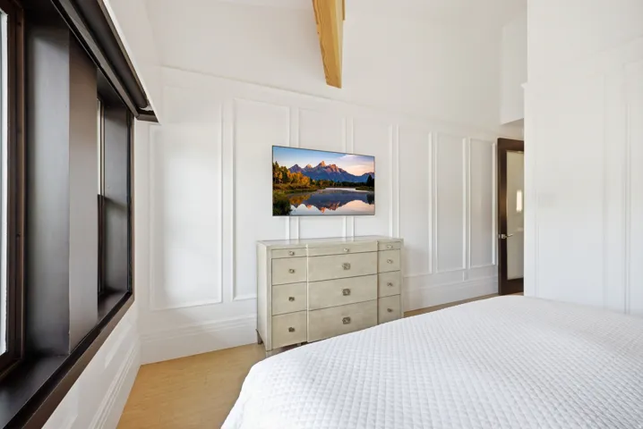 Vaulted ceiling with exposed wood beam, wide plank wood-finish flooring, and elegant wainscoting paneling