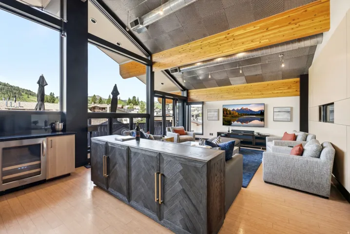 Open-concept living area featuring a vaulted ceiling with exposed wood beams and a metal grid finish