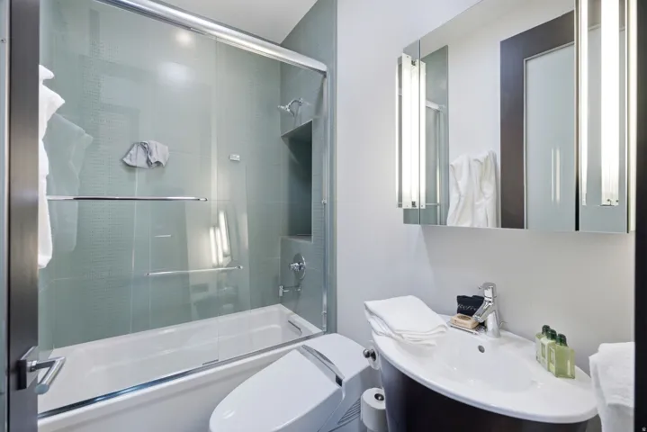 Modern bathroom featuring a built-in tub with glass sliding doors, integrated shower niche, a wall-mounted medicine cabinet with integrated lighting, and a contemporary vanity with an undermount sink