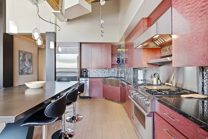 Gourmet kitchen featuring deep red cabinetry, black granite countertops, a built-in stainless steel oven range, a stainless steel farmhouse sink, and a mosaic tile backsplash