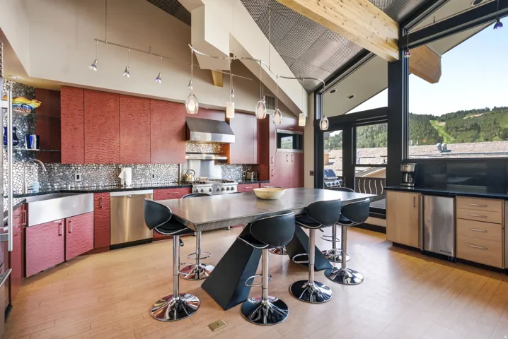 Modern kitchen featuring a large central island, stainless steel appliances, red wood-finish cabinetry, a textured backsplash, and expansive windows