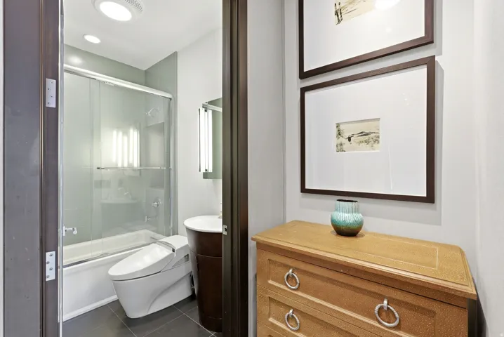 Modern bathroom featuring a sliding glass shower door over the tub, contemporary vanity with vessel sink, and large format floor tiles