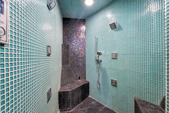 Shower enclosure featuring full-height teal mosaic tiling, a built-in bench, and a handheld shower fixture
