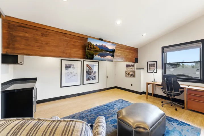 Vaulted ceiling room featuring light-toned flooring, a built-in wet bar with a dark countertop and under-counter refrigeration, and a prominent wood-paneled beam