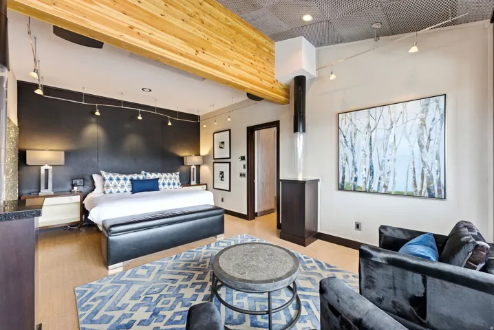Bedroom featuring wood-finish flooring, exposed wood beam ceiling, track lighting, a dark accent wall, and a built-in vertical water feature