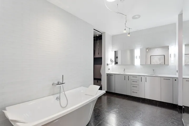 Freestanding soaking tub with chrome fixtures, set against a white tiled wall