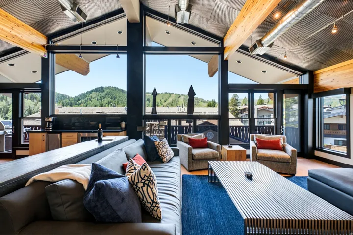 Spacious living area featuring expansive windows, exposed wood beams, and a vaulted ceiling