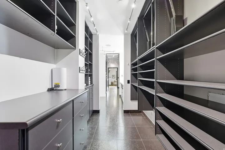 Expansive custom closet system featuring extensive shelving, integrated drawers, track lighting, and durable tile flooring