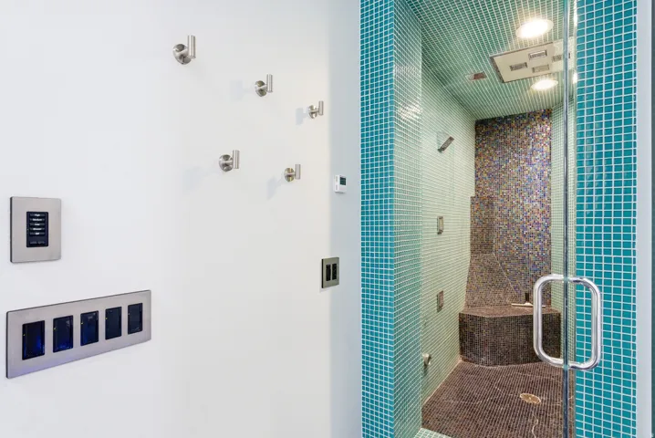 Tiled shower enclosure featuring a glass door and multiple shower heads