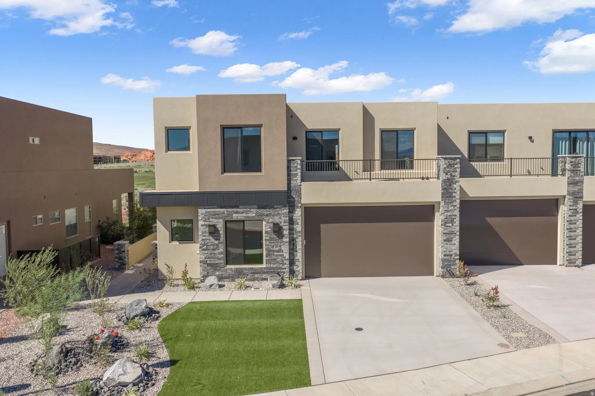Modern stucco exterior with stacked stone accents, dark-framed windows, an integrated garage, and a second-level balcony