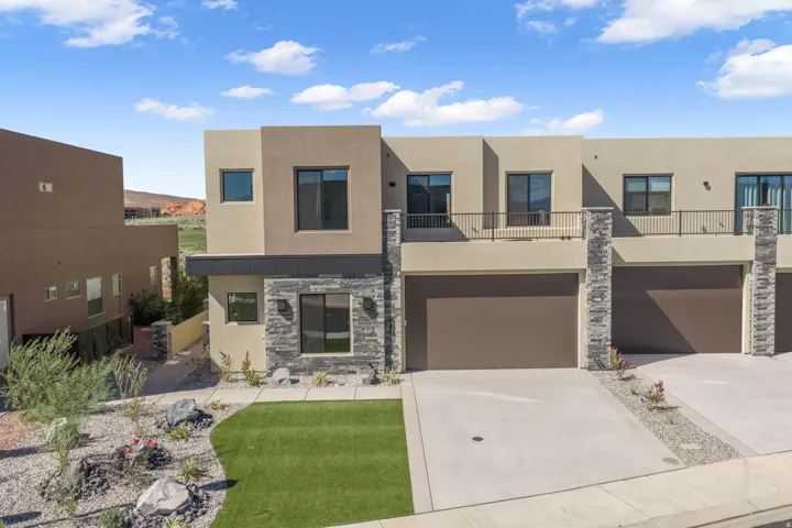 Modern stucco exterior with stacked stone accents, dark-framed windows, an integrated garage, and a second-level balcony