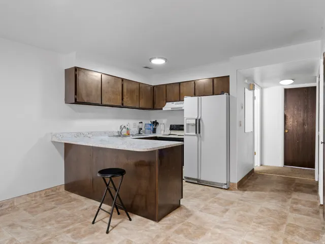 Kitchen featuring a peninsula, light countertops, white fridge with ice dispenser, a kitchen breakfast bar, and dark wood finish cabinetry