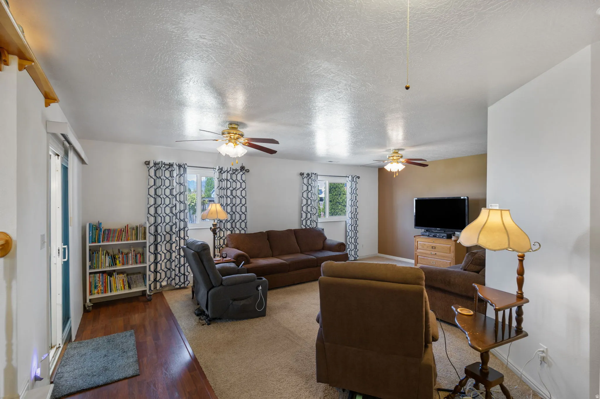 Living area with plenty of natural light, a textured ceiling, wood finished floors, and ceiling fan