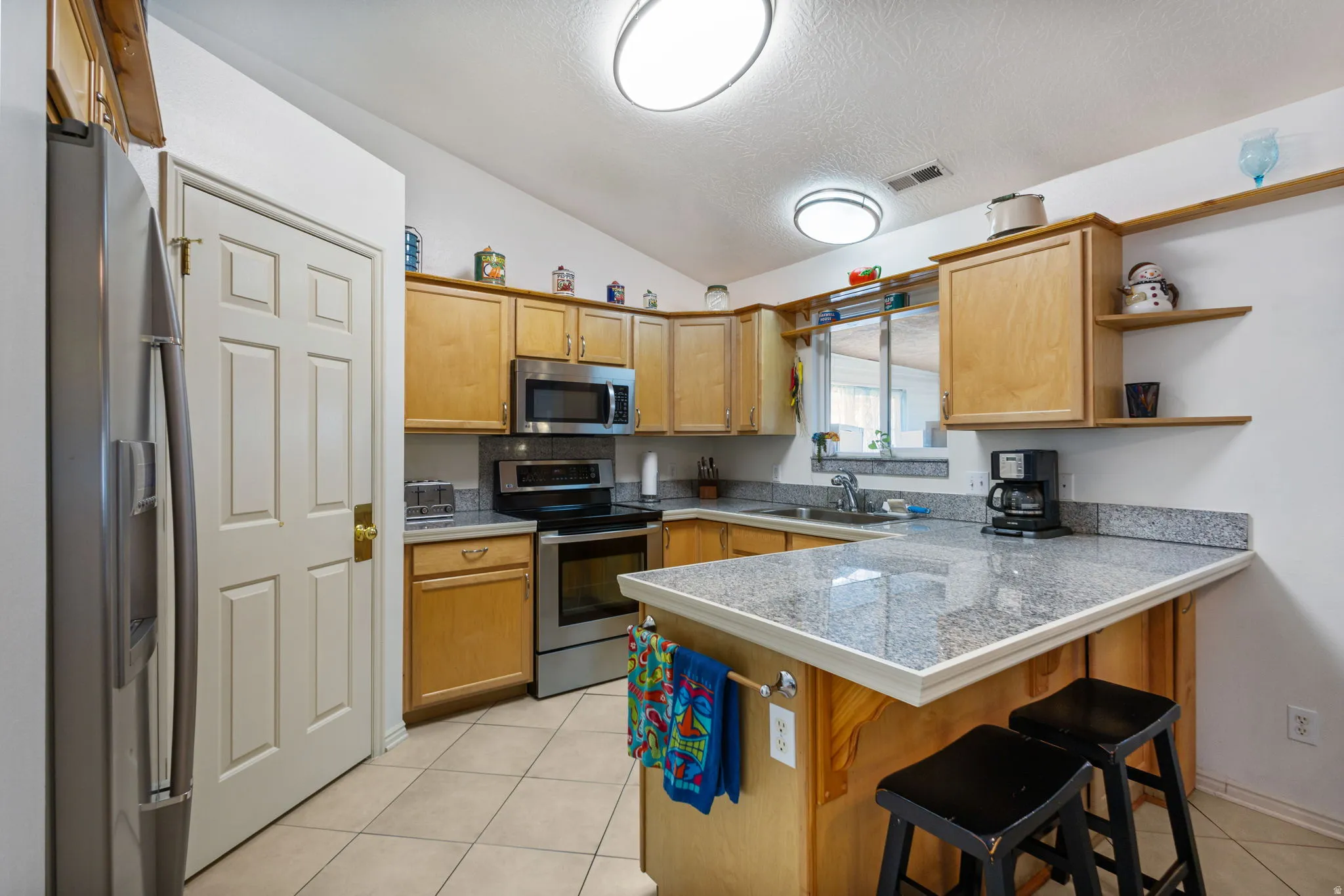 Kitchen featuring stainless steel appliances, a breakfast bar, a peninsula, tile countertops, and wood finish cabinetry