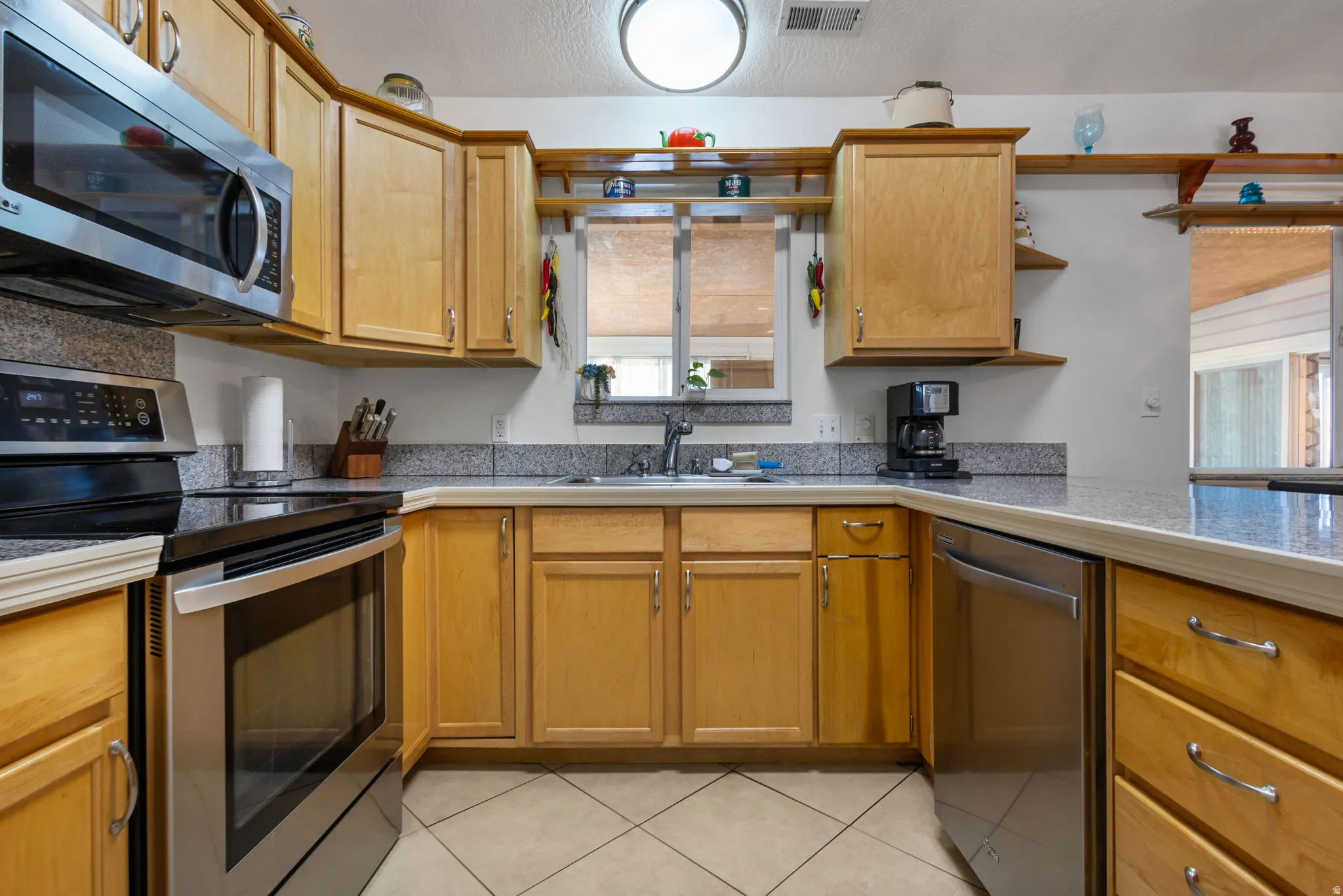 Kitchen featuring stainless steel appliances, a textured ceiling, tile counters, light tile patterned floors, and wood finish cabinets