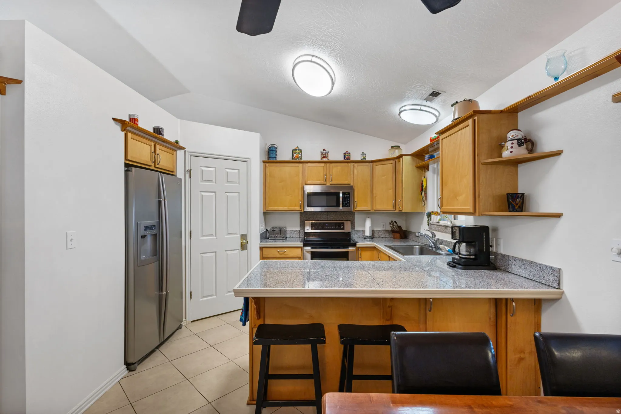 Kitchen featuring a peninsula, stainless steel appliances, ceiling fan, a breakfast bar, and open shelves