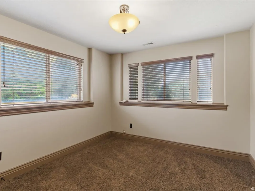 Carpeted room featuring multiple windows with blinds, a flush mount ceiling light fixture, and crown molding