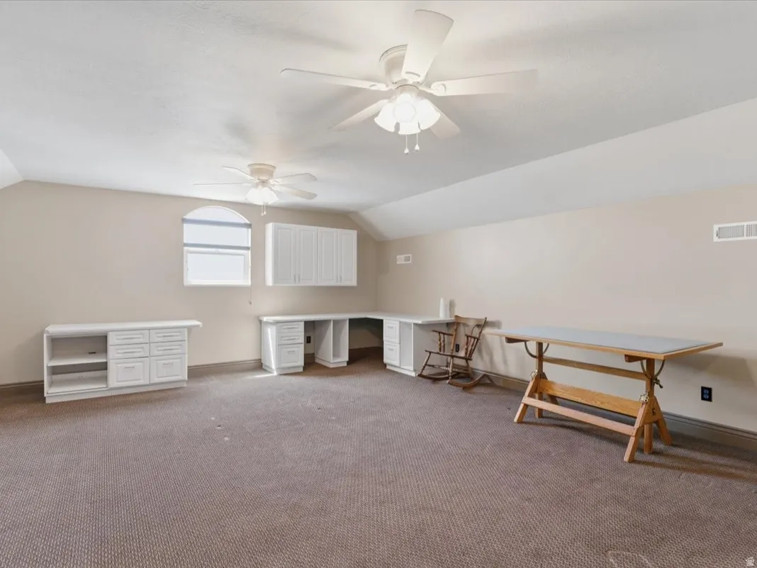 Spacious room featuring carpeting, two ceiling fans, built-in white cabinetry, a built-in white desk with drawers, and an arched window