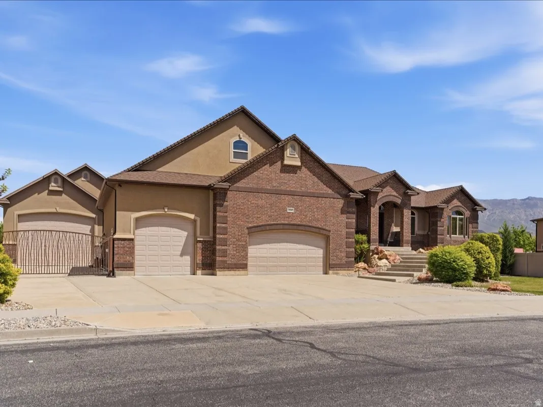 Spacious residence featuring a brick and stucco exterior, multiple garage bays with arched entrances, a covered entry porch with columns, a terraced front walkway, and mature landscaping