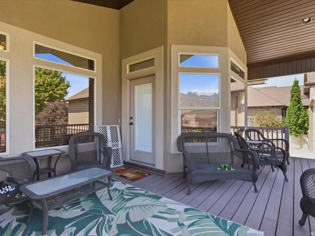 Covered outdoor deck featuring composite decking, recessed lighting, expansive windows, and a glass-paneled door