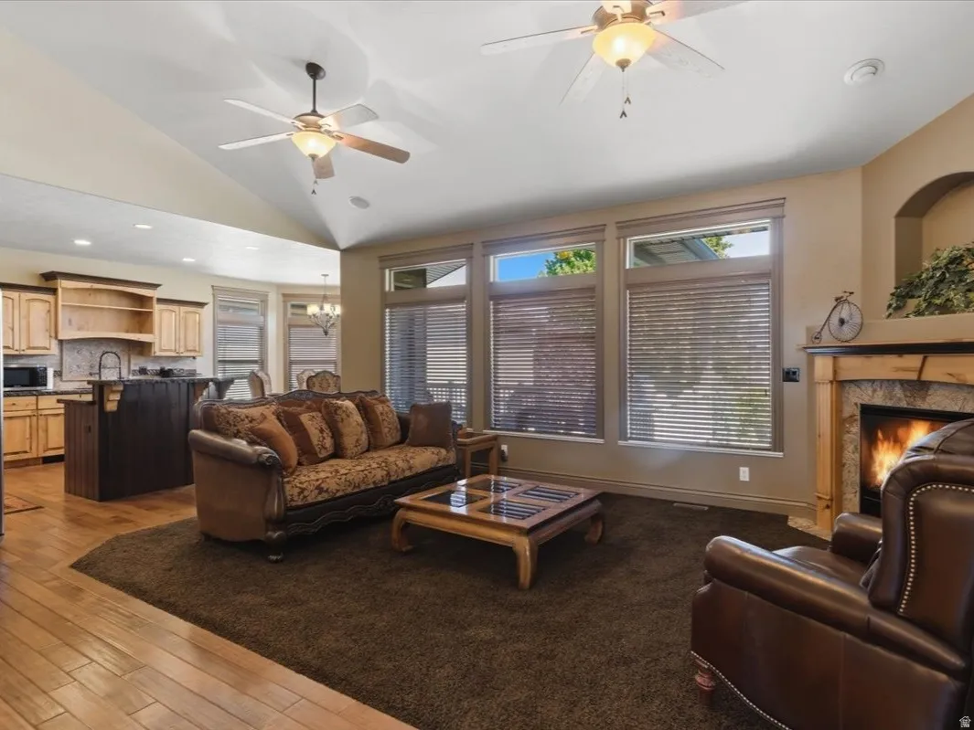 Living area featuring a stone surround fireplace with wood mantel, vaulted ceilings, and ceiling fans with light fixtures