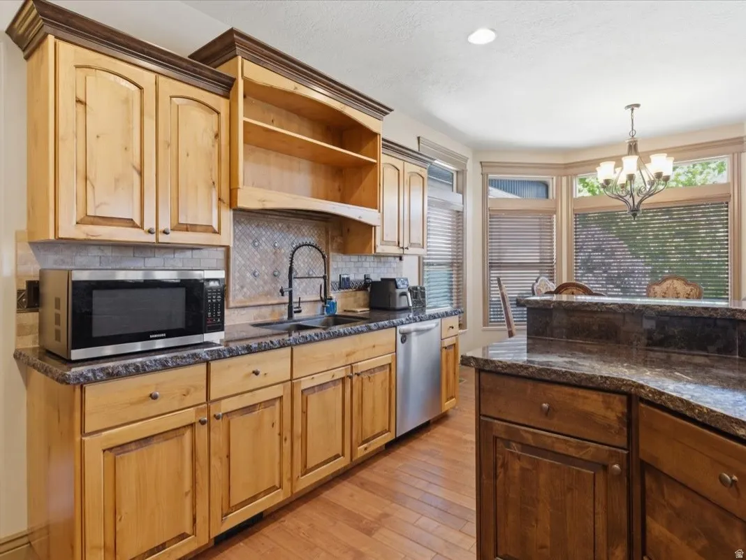 Kitchen featuring natural wood cabinetry, stone countertops, a mosaic tile backsplash, and stainless steel appliances